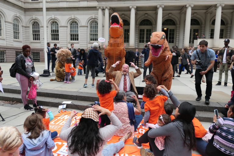 two dinosaurs roaring at a storytime on the steps of city hall