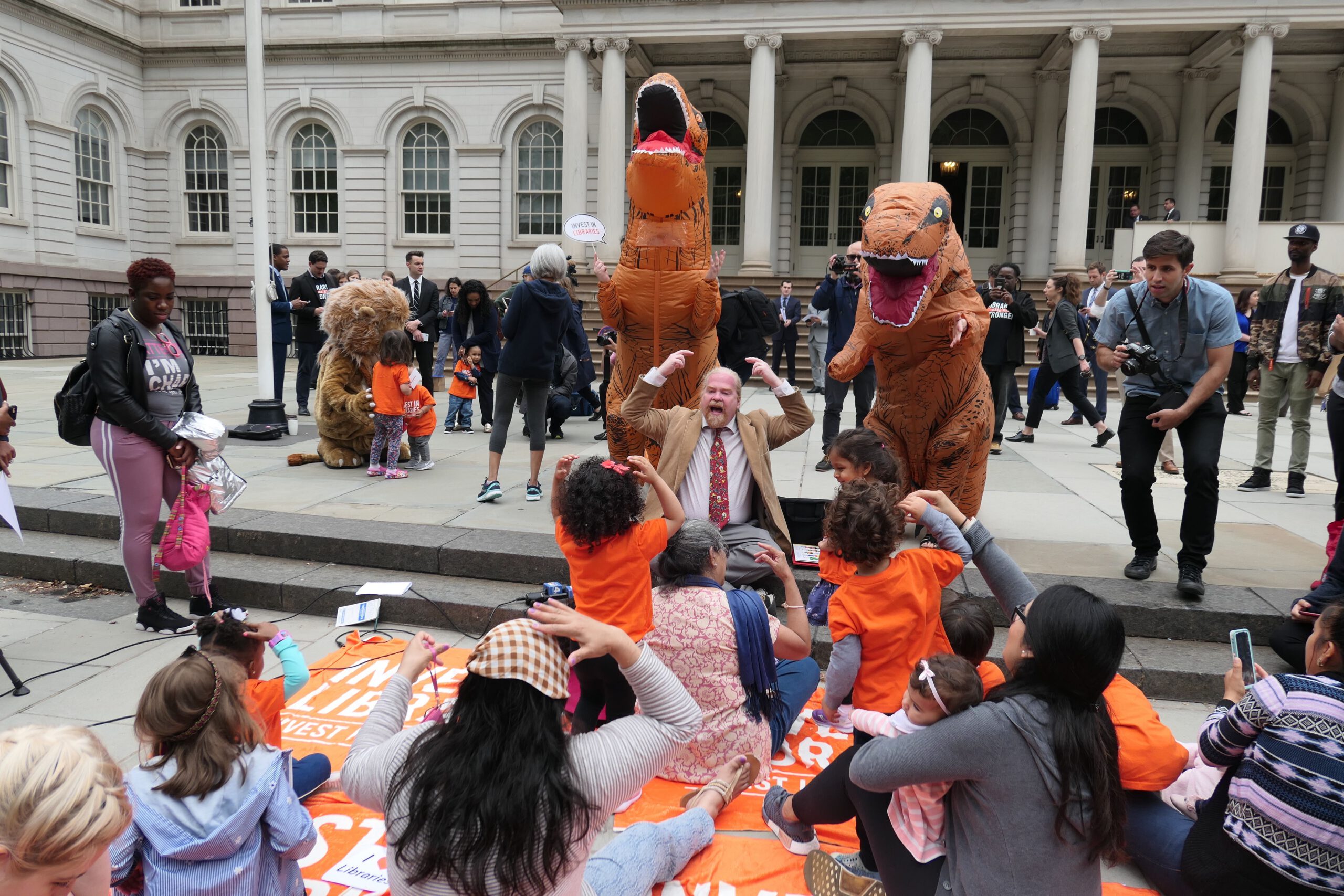 two dinosaurs roaring at a storytime on the steps of city hall