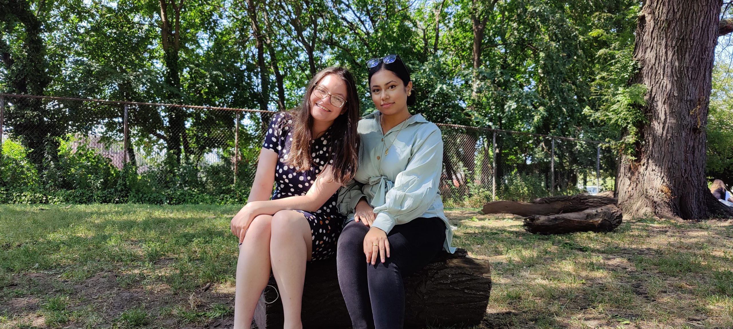 Two young women sitting on a log in the park