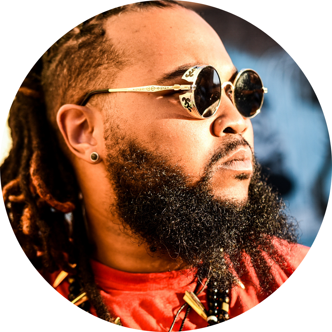 Kyle Ramsey being very very cool with dreadlocks wearing sunglasses and a red shirt
