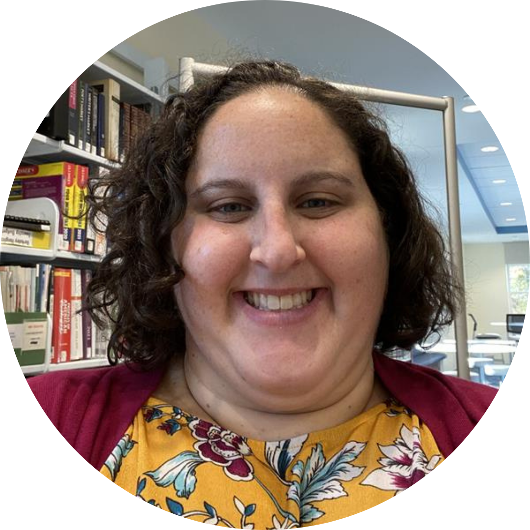 Rachel Talbert, a person with curly hair is smiling in front of a bookshelf