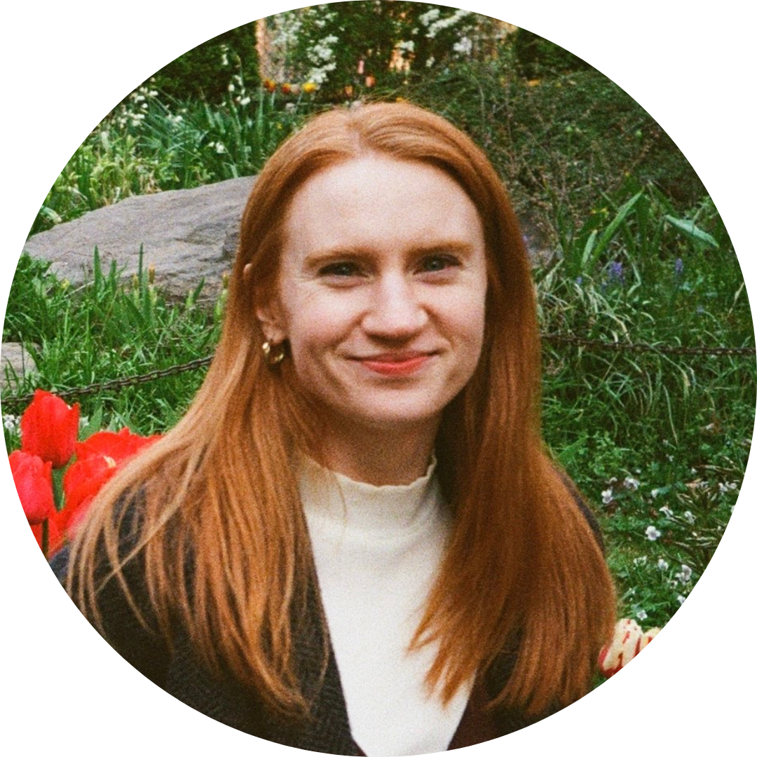 Sarah Healy, a person with red hair, standing in front of flowers