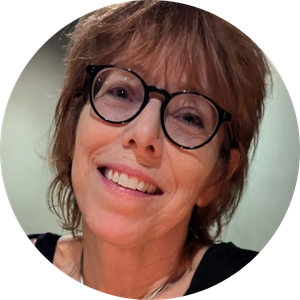 Headshot of a smiling woman with short reddish-brown hair, wearing round glasses and a black top.