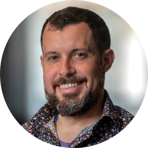 Headshot of a smiling man with short hair and a beard, wearing a floral-patterned button-down shirt.