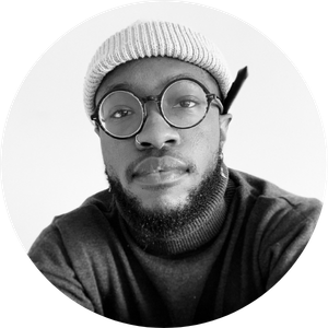 Black-and-white headshot of a man wearing a beanie, round glasses, and a beard, with a neutral expression.