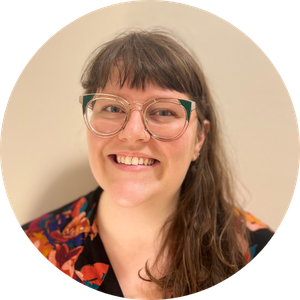 Headshot of a smiling woman with long hair and bangs, wearing colorful glasses and a floral-print top.