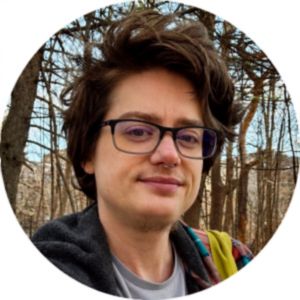 A person wearing glasses and a backpack in a wooded area.
